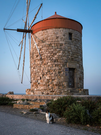 Rhodes, Greece - May 27, 2023: Windmill of Mandraki at sunset. A cat sitting in front of the mill.のeditorial素材