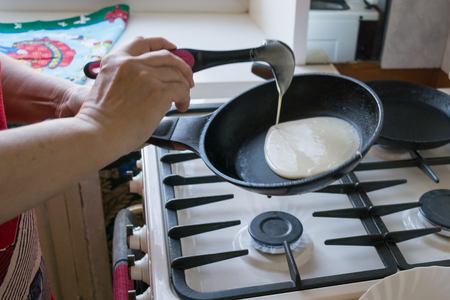 the dough spreads in a pan for baking pancakes in the hands of an elderly womanの写真素材