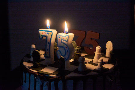candles burning on a birthday cake with chocolate icing, chess pieces, the number 75.
