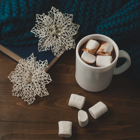 cozy winter home background - cup of hot cocoa with marshmallow, Christmas  snowflakes and warm blue knitted sweater, book on wooden table.の写真素材