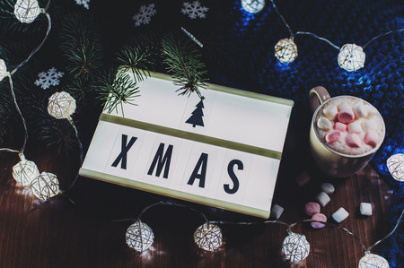 Winter composition - light board with text xmas, branch of a Christmas tree, snowflakes, garland blue warm knitted sweater on a wooden table.の写真素材