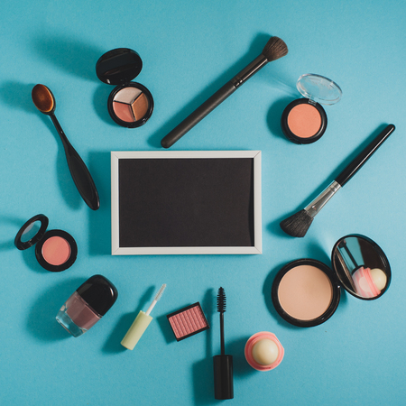 Cosmetics - powder, blush, brushes, mascara, shadows on a blue background. In the center is a black board for text. Beauty blog concept.の写真素材