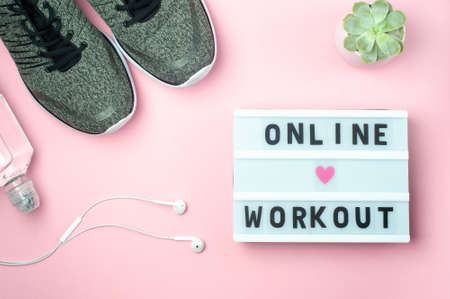 Online Workout - text on display lightbox on pink background. Flat lay - Sneakers, a bottle of water, white headphones. Sport concept.の写真素材