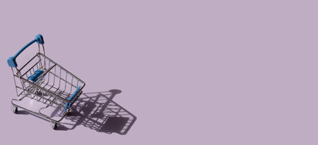 Miniature supermarket trolley on purple background. Place for text.