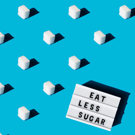 Eat less sugar - text on lightbox display. Refined sugar pattern on a blue background. Concept of...