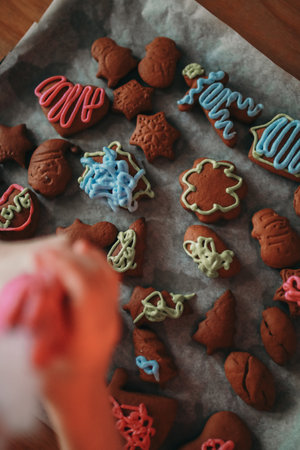 Close-up of child's hands making gingerbread cookies for Christmas. Child is decorating gingerbread cookies with pink icing using a piping bag. There are various other cookies.の写真素材