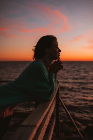 A silhouette of a woman leaning on a wooden railingの写真素材
