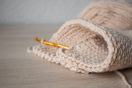 A crochet with beige yarn and an orange hook on a wooden surfaceの写真素材