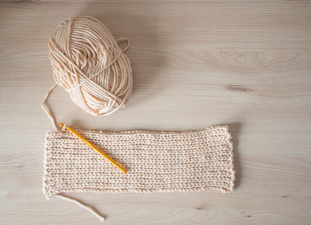 A crochet with beige yarn and an orange hook on a wooden surface