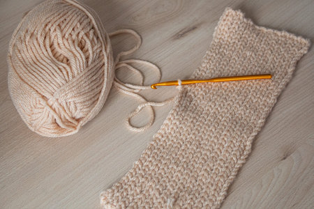 A crochet with beige yarn and an orange hook on a wooden surface