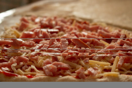 A close-up of an uncooked pizza topped with shredded cheese and diced hamの写真素材
