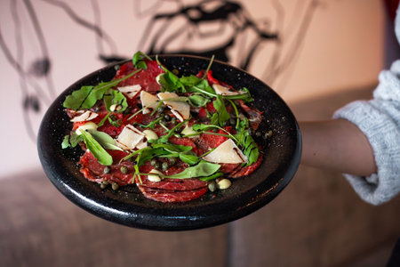 A black plate with beef carpaccio topped with arugula, parmesan shavings, capersの写真素材