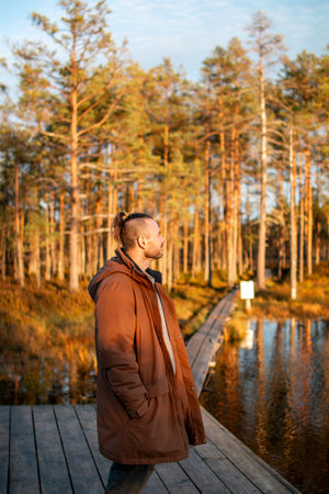 A man in a brown coat stands on a wooden dock by a calm lakeの写真素材