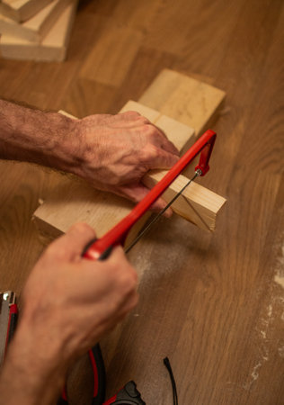 A person is sawing a wooden block with a red-handled hacksaw on a wooden surfaceの写真素材