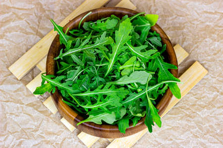Top view of fresh green spicy arugula salad leaves in brown wooden bowl on light background.の写真素材