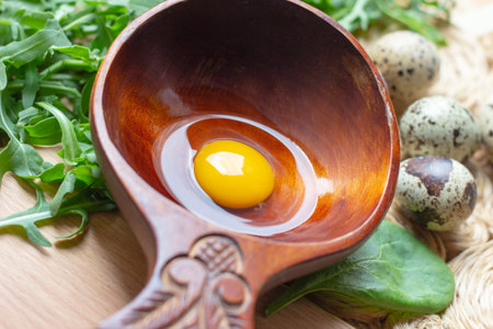 Fresh raw quail eggs in wooden spoon with arugula and spinach salad leaves on rustic straw and...