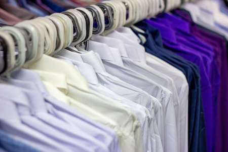 Many different colorful clothes on a hanging rack in the retail shop store. Soft selective focus photographyの写真素材