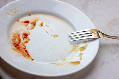 White dirty and empty dish with fork on wooden table.の写真素材