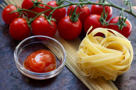 Tomato ketchup sauce in a bowl with cherry tomatoes and raw pasta aside on rusty metal background.の写真素材