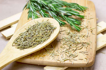 Bright fresh green and dried rosemary branches, twigs and leaves in a wooden spoon and on a board on light background.の写真素材