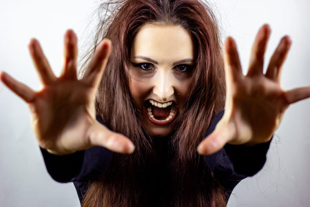 Angry, stressed, frightened and screaming mad young woman in black against light background
