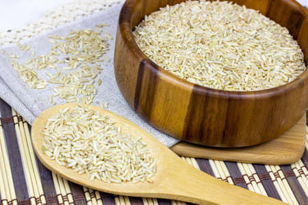 Uncooked brown rice in a bowl and spoon with light napkin on wooden backgroundの写真素材