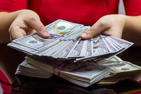 Woman in red dress holdind and counting cash money (american dollars) in her hands on black table...