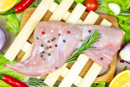 Top view of raw uncooked pink rabbit leg meat with green rosemary and fresh vegetables on light wooden cutting board background.の写真素材