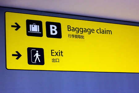 Bright illuminated yellow and black airport signs with arrows and plane icons and the title in Chinese: "Baggage claim" and "Exit".の写真素材