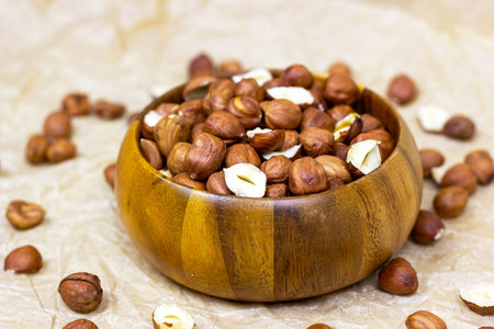 Peeled brown hazelnuts in round wooden bowl on light background.