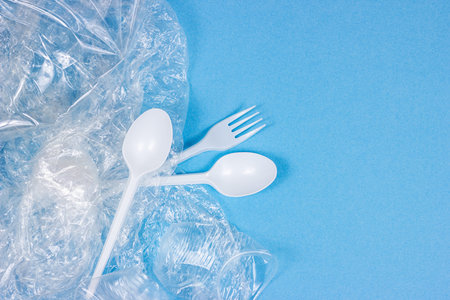 Top view of crushed plastic spoons, forks, bottles and cups as a disposable waste with copy space on...