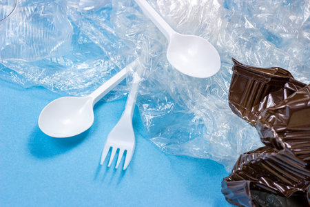 Crushed plastic spoons, forks, bottles and cups as a disposable waste on bright blue background....