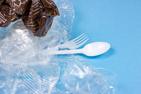 Crushed plastic spoons, forks, bottles and cups as a disposable waste on bright blue background....