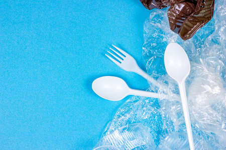 Top view of crushed plastic spoons, forks and cups as a disposable waste with copy space on bright blue background. Environmental pollution and litter recycling concept.の写真素材