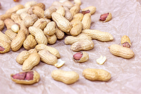 Raw unpeeled peanut nuts in nutshell on light paper background.