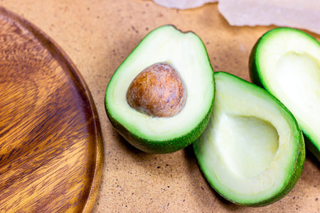 Fresh half sliced green avocado pieces ready to eat on brown wooden board background.