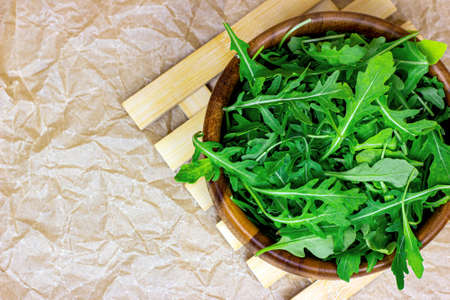 Top view of fresh green spicy arugula salad leaves in brown wooden bowl on light background.の写真素材