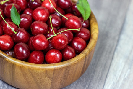 Fresh juicy red sweet cherry berries in the wooden bowl on light background in summer.