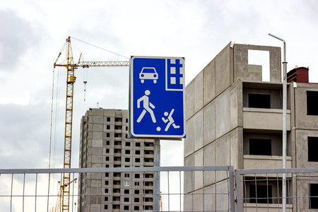 Construction site with high crane, gray block building house and blue and white living sector road...