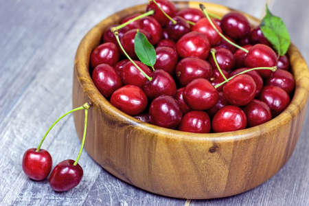 Fresh juicy red sweet cherry berries in the wooden bowl on light background in summer.の写真素材