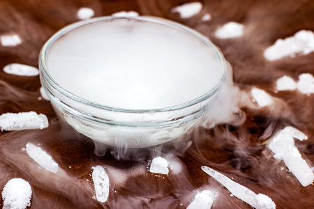 White cool dry ice (frozen carbon dioxide) with smoke effect in the glass bowl on the dark brown...