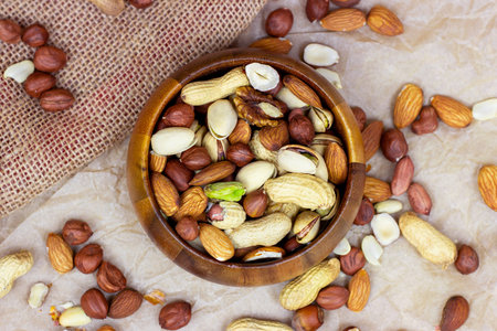 Top view of different nuts: almonds, pistachios, peanuts, hazelnuts in wooden bowl on light...