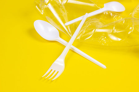 Plastic spoons, forks, bottles and cups as a disposable waste on bright yellow background. Environmental pollution and litter recycling concept.の写真素材