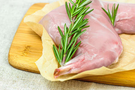 Raw uncooked pink rabbit leg meat with green rosemary and fresh vegetables on light wooden cutting board background.の写真素材