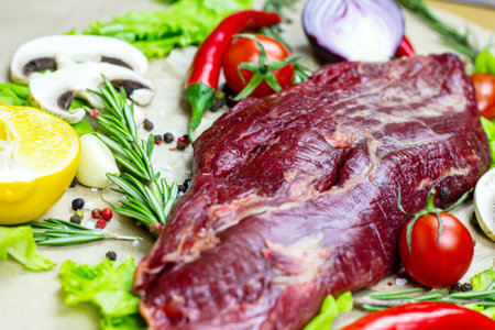 Raw red beef meat with green rosemary and fresh vegetables on light wooden cutting board background.の写真素材