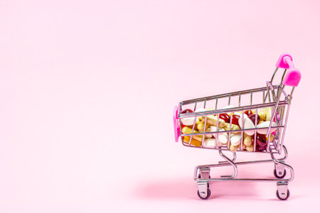 Shopping cart with different medical pills and capsules in it on pink background. Pharmacology and drugstore concept.の写真素材
