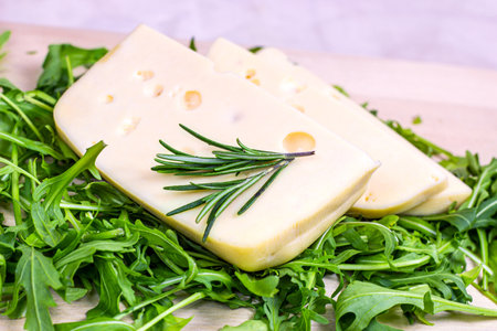 Maasdam cheese slices with green arugula leaves on light wooden background.の写真素材