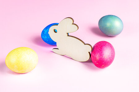 Funny wooden Easter Bunny with colorful eggs as symbols of a holiday on light pink background.の写真素材