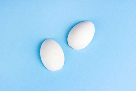 Two white wooden eggs on bright light blue background.の写真素材