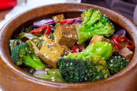 Homemade vegetarian fried tofu with vegetables (broccoli, pepper, onions and green beans) in the wooden bowl.の写真素材